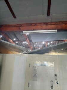 Blick auf das beschädigte Hallendach über dem Kühlraum, Tageslicht fällt durch die Einschläge im Eternit